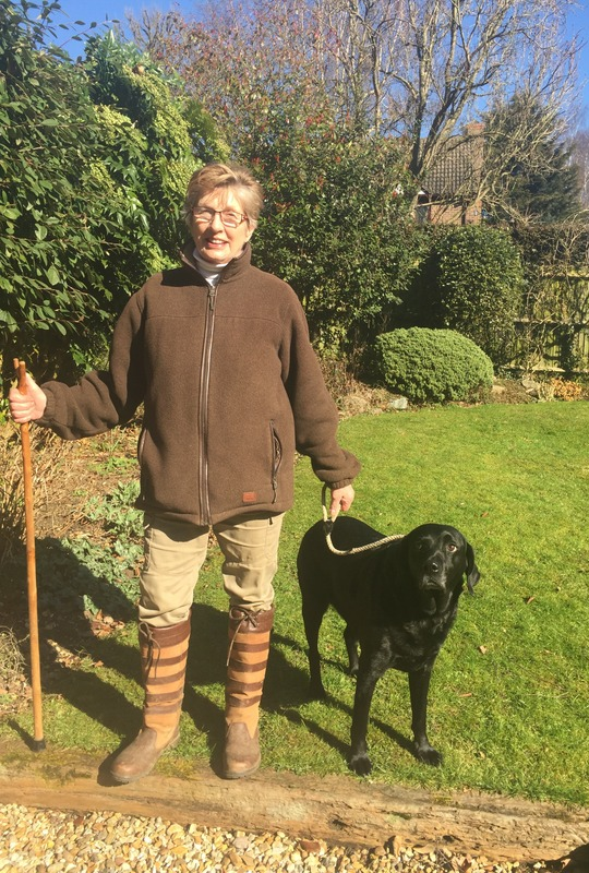 Linda, standing in her garden with a black labrador by her side.